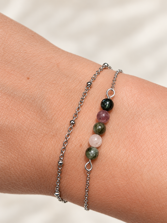 Bracelet double rang argenté porté au poignet, avec une chaîne à petites billes et un rang de perles colorées.